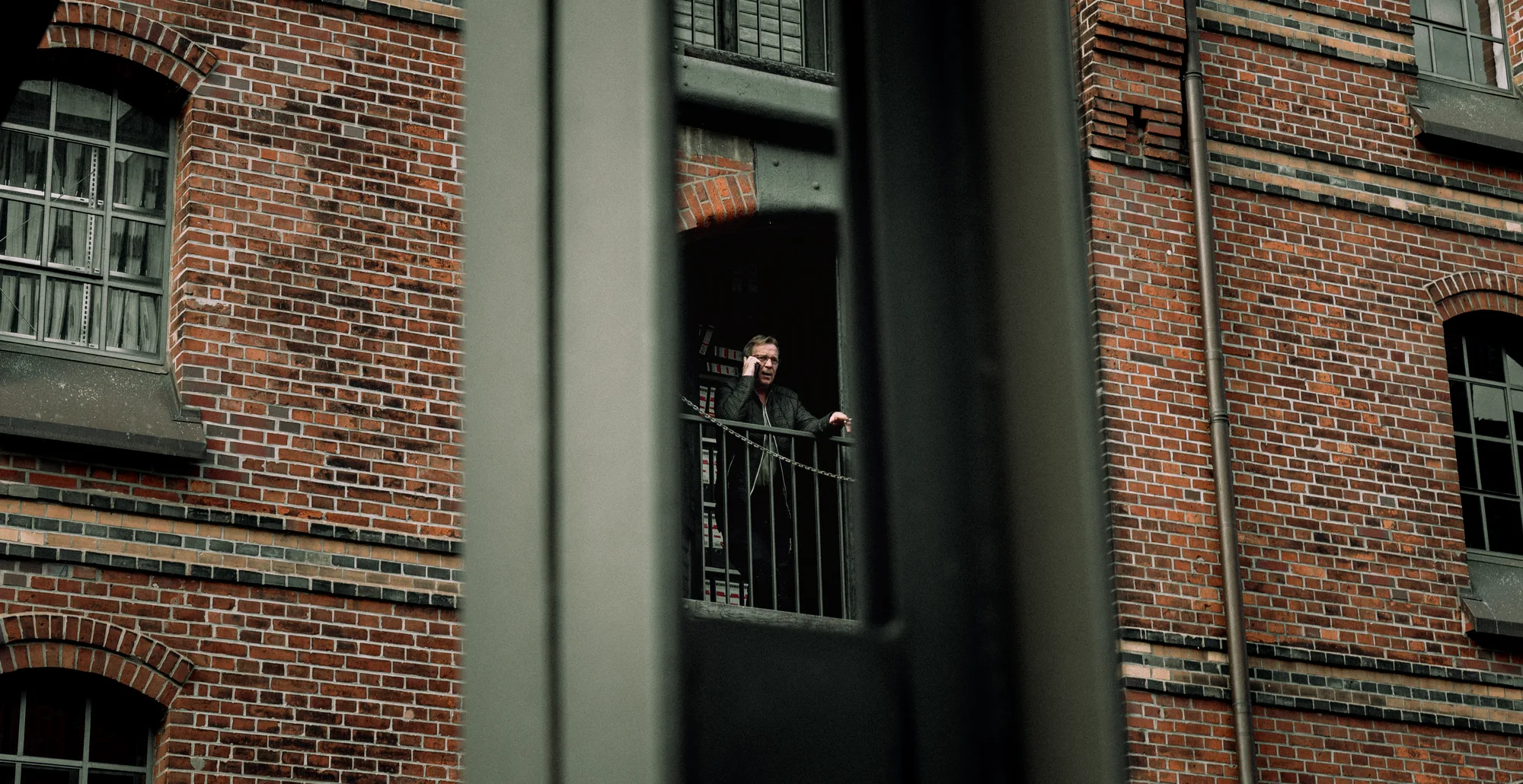 A man on the phone on a warehouse balcony, seen between steel beams