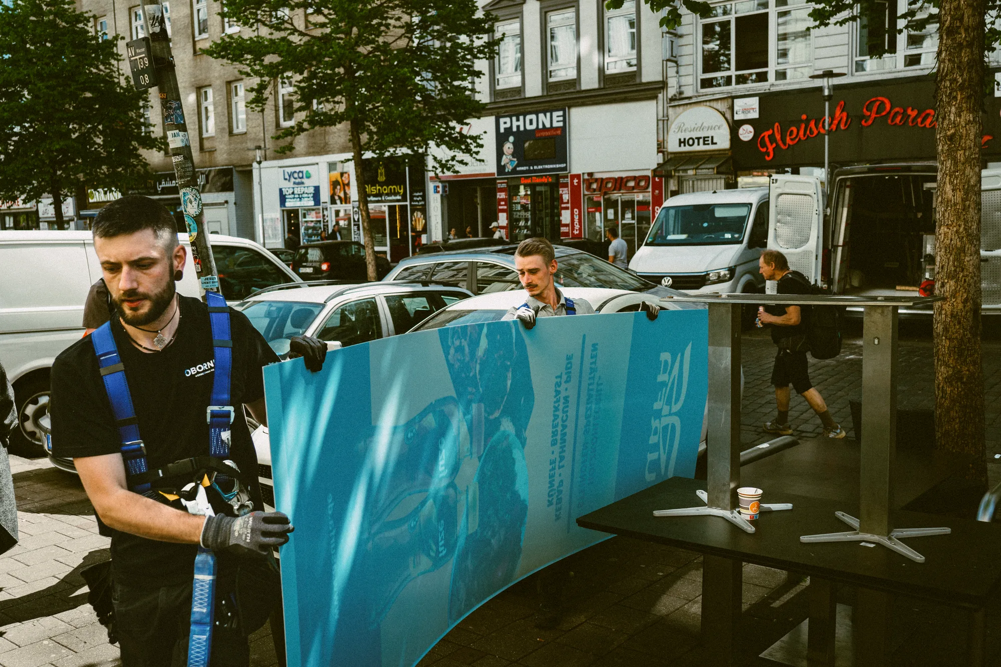 Two workers carrying a large printed panel across a busy street