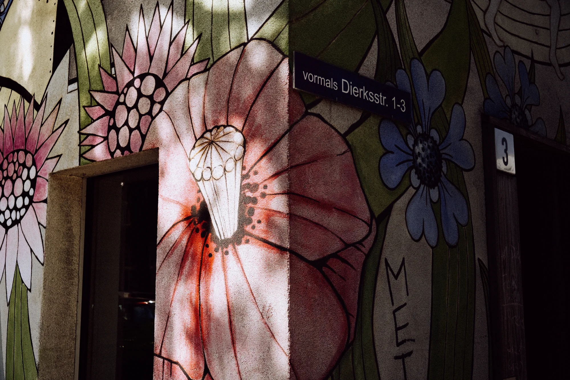 A large painted flower mural around a doorway, with an old street sign