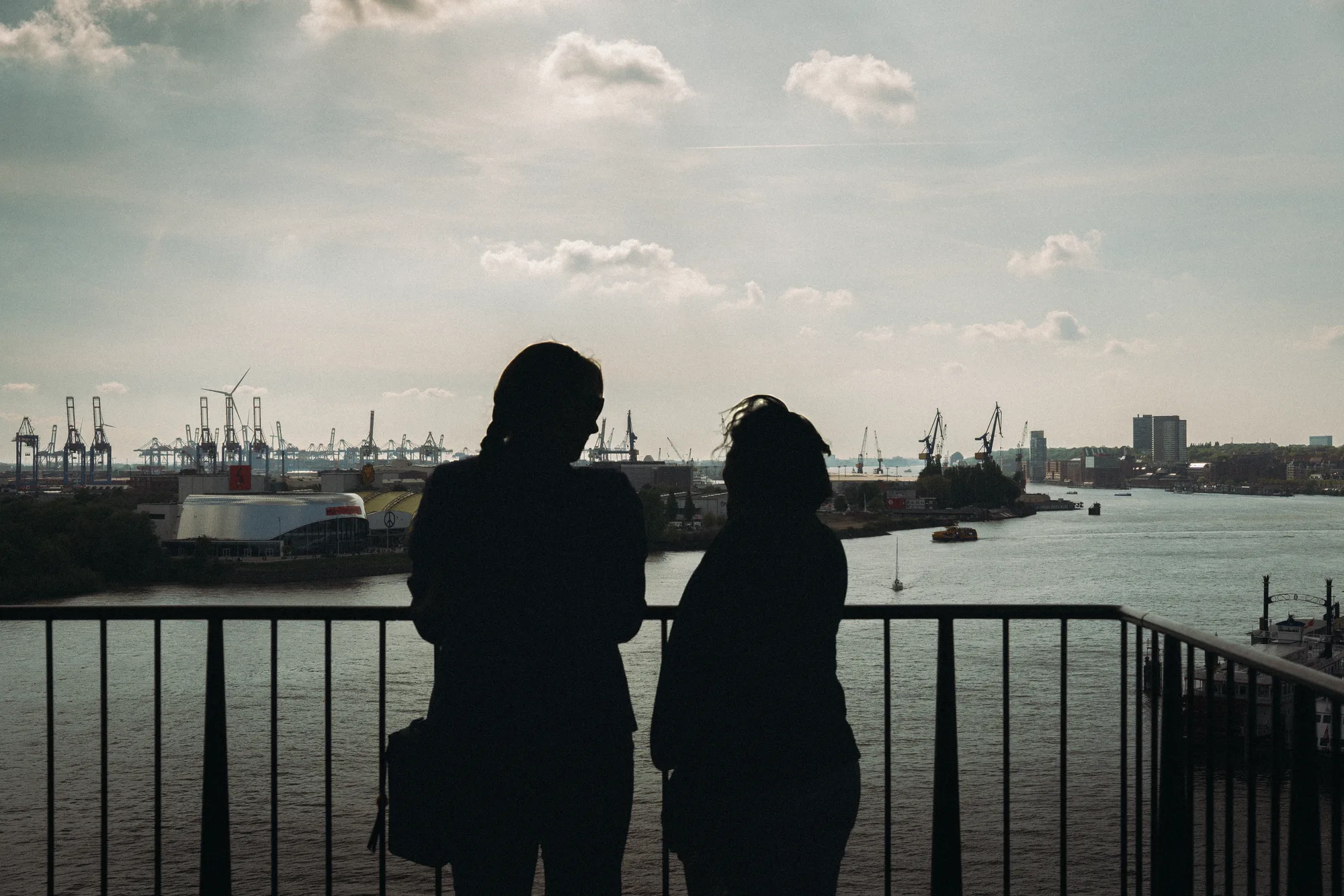 Two women in silhouette at a railing above the harbour
