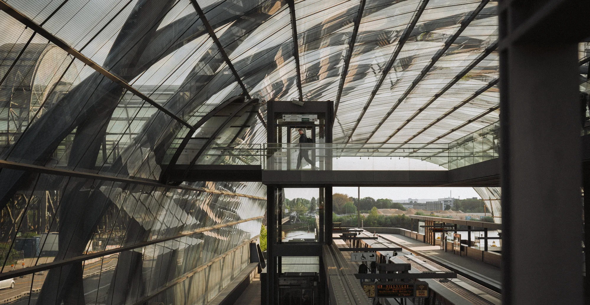 A man crossing a glass walkway under the curved roof of a station