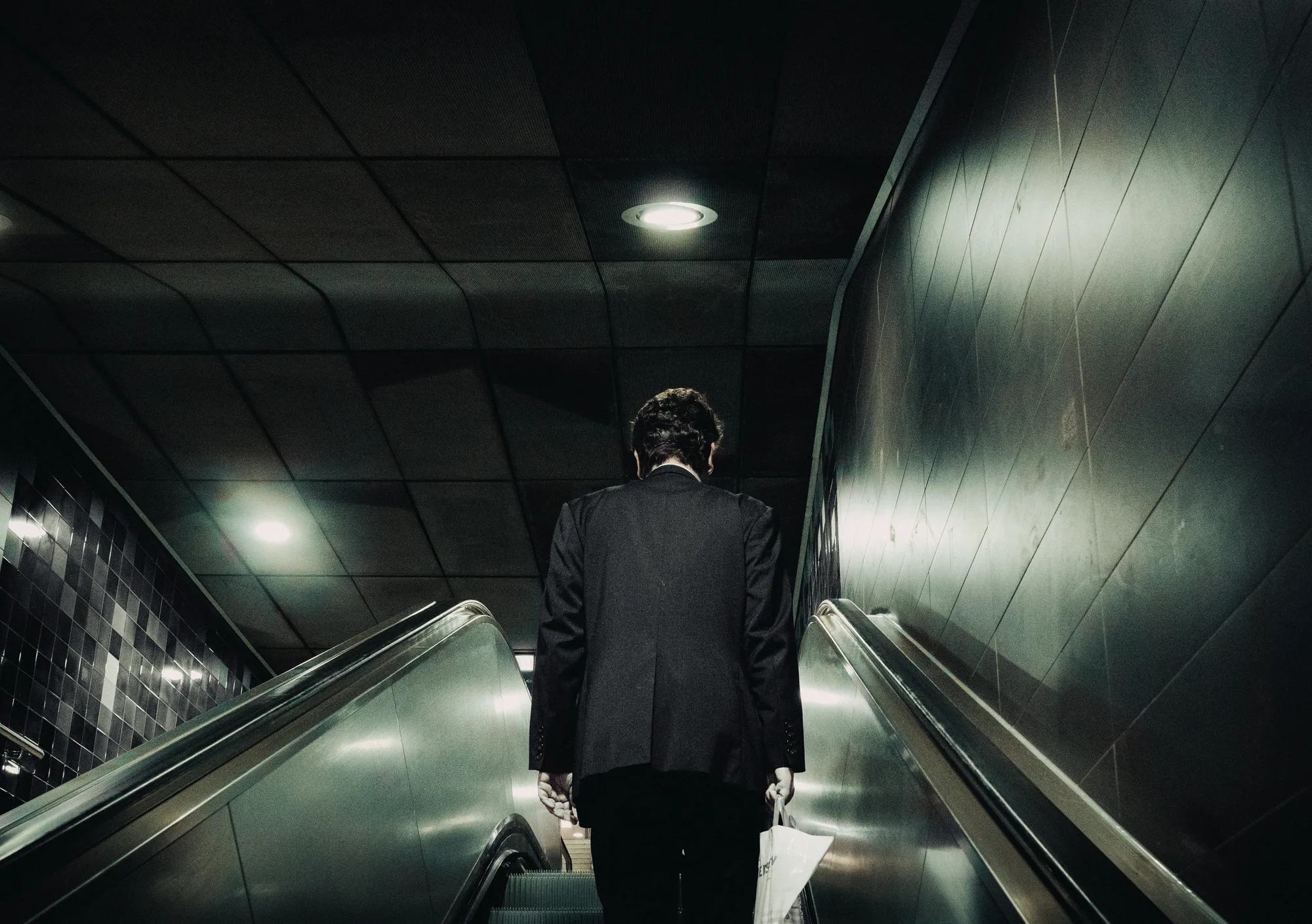 A man in a suit riding an escalator down into a dark station