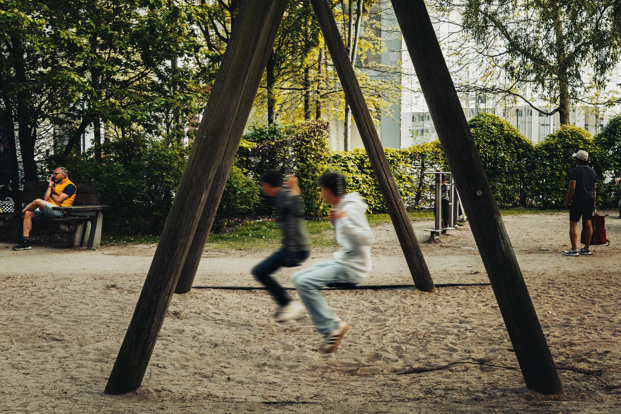 Two children on a swing in a park, a man on a bench behind them