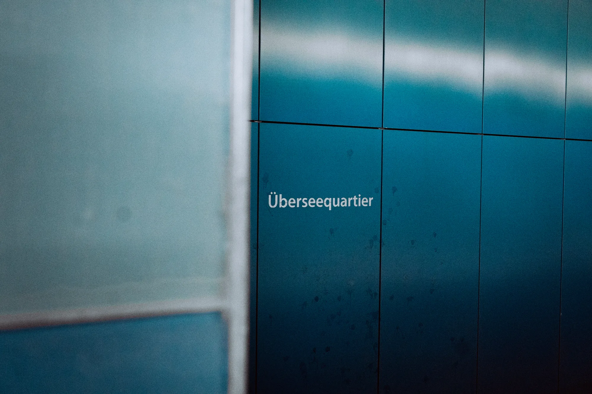 The Überseequartier station sign on blue metal panels, softly out of focus
