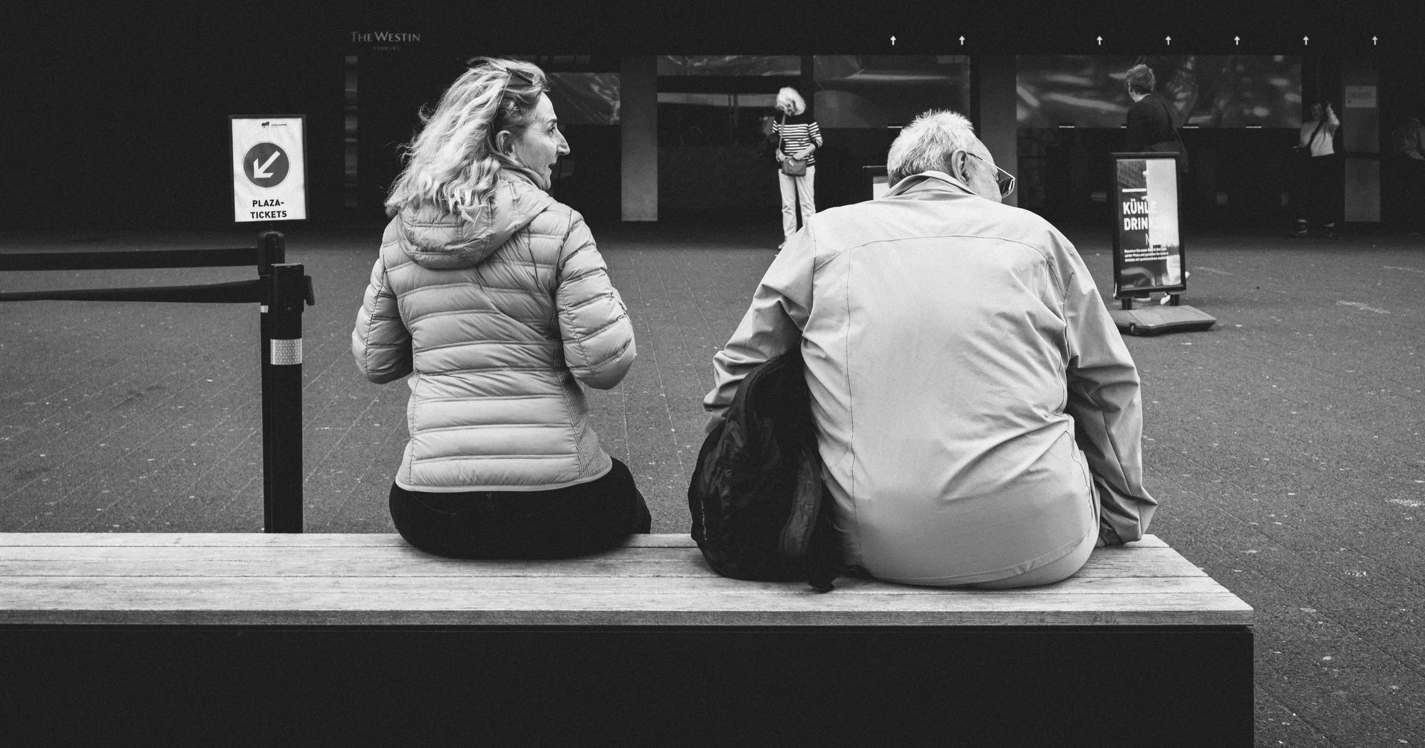 A woman and a man seen from behind on a wooden bench, the woman turning to talk