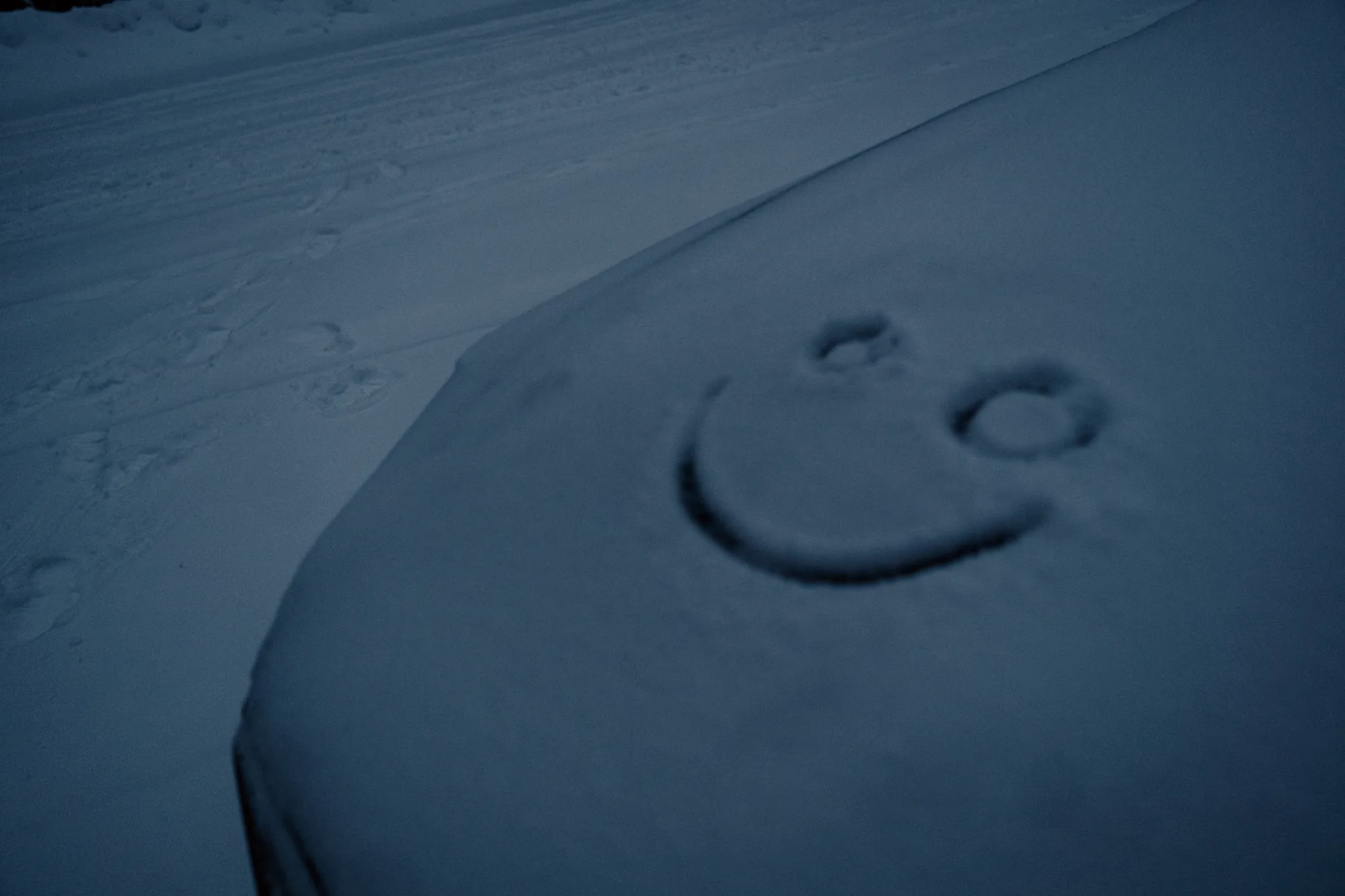 A smiley face drawn in the snow on the bonnet of a car