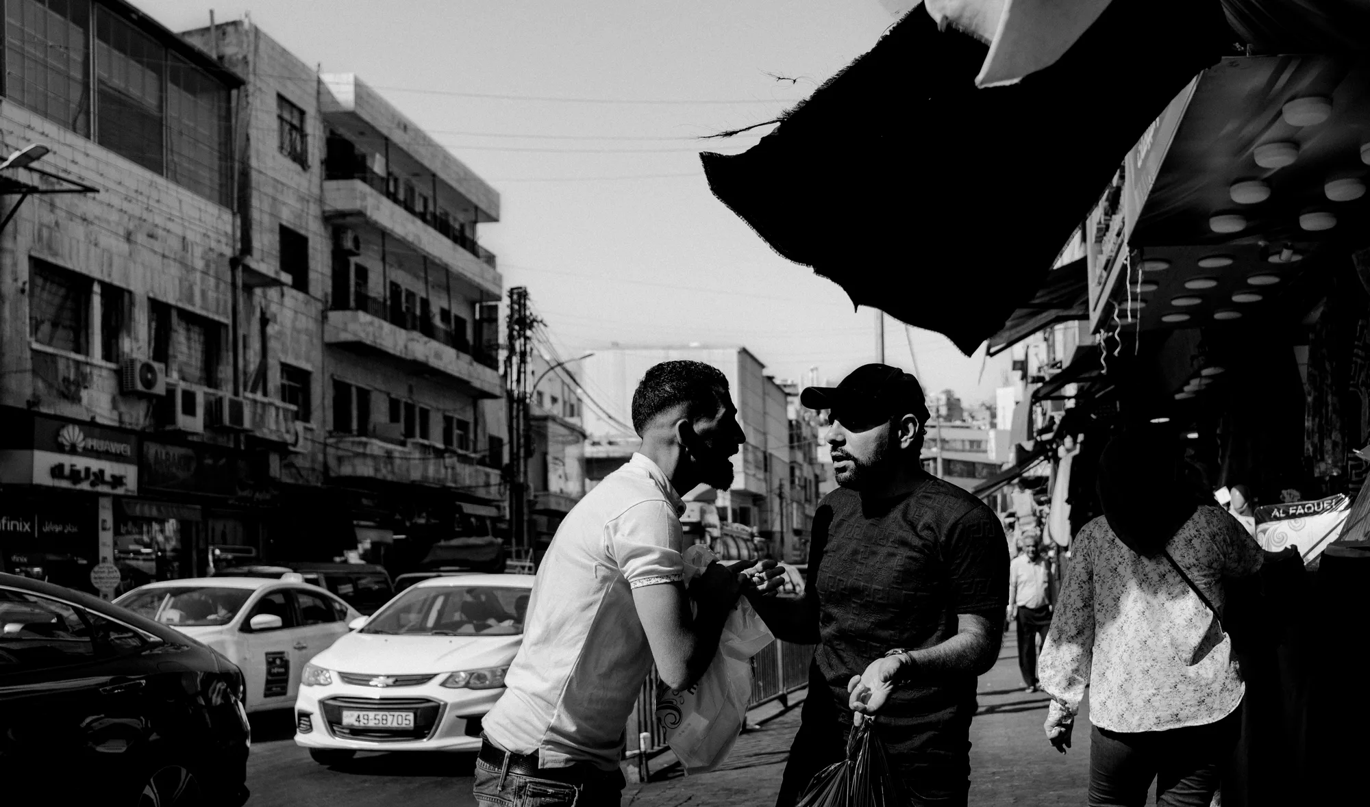 Two men arguing in a busy Amman street under a torn awning