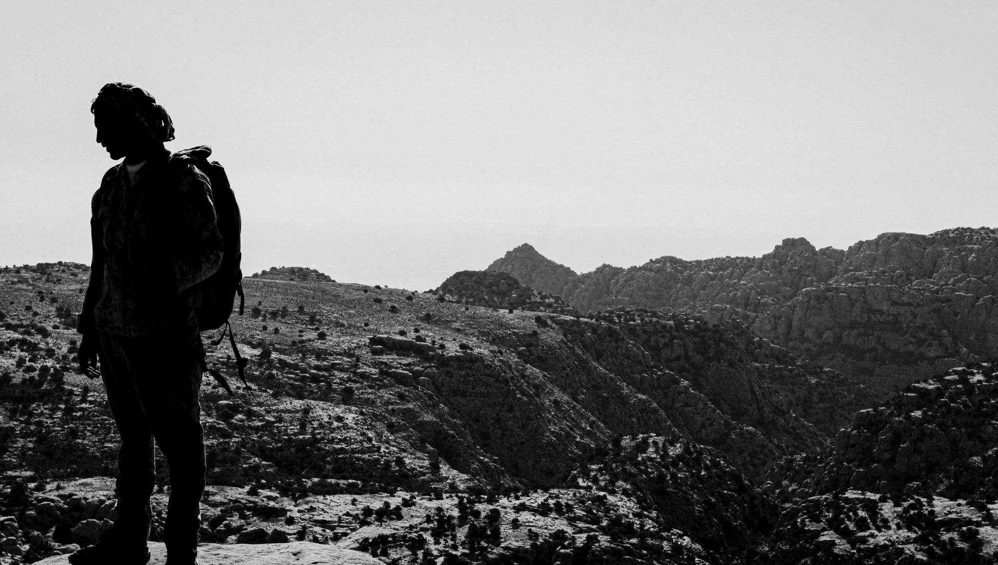 A man with a backpack in silhouette above the canyons of Dana