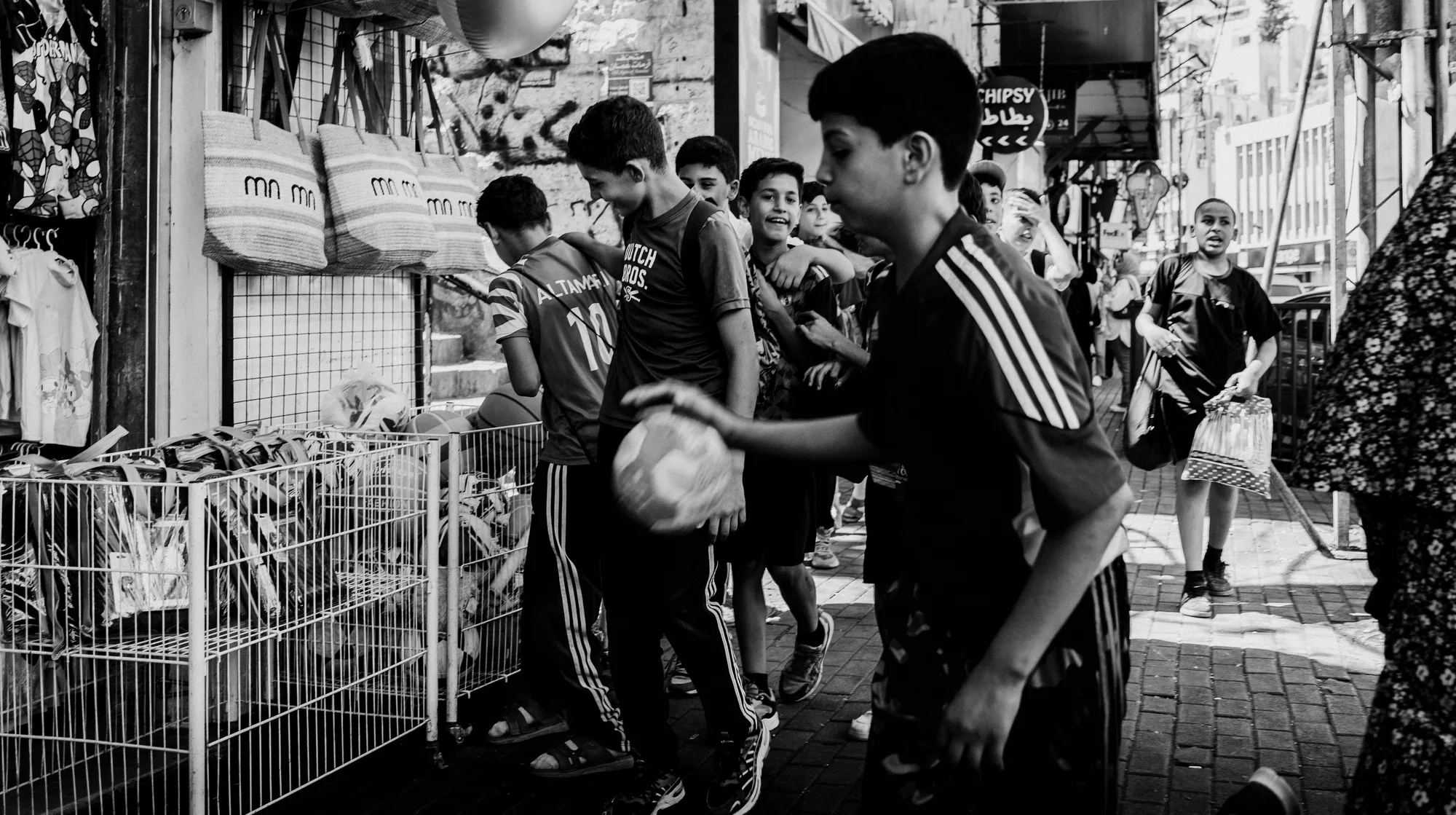 Boys in football shirts crowding along a shopfront in Amman, one bouncing a ball