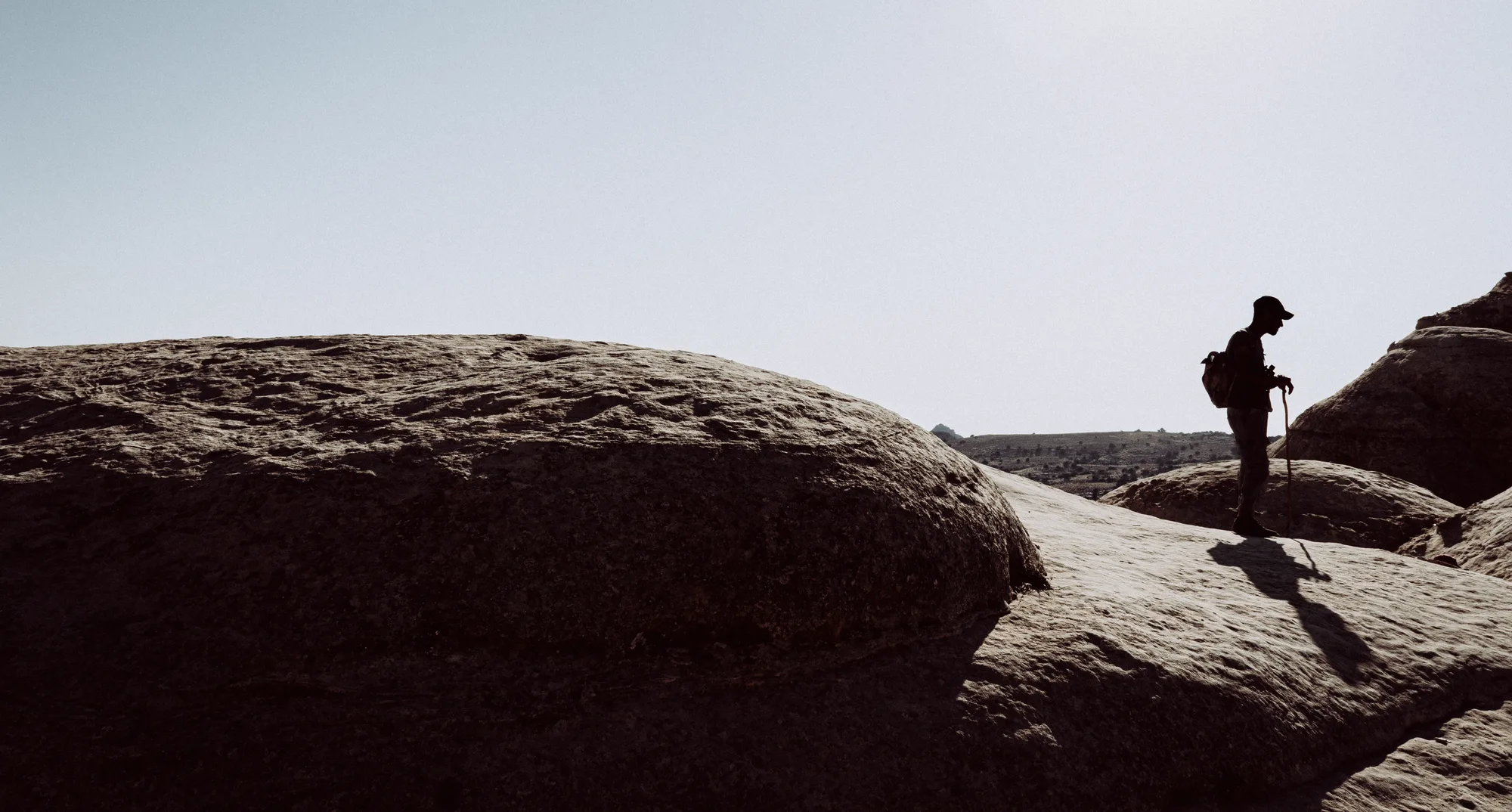 A hiker with a walking stick in silhouette on smooth sandstone, his shadow stretching behind him