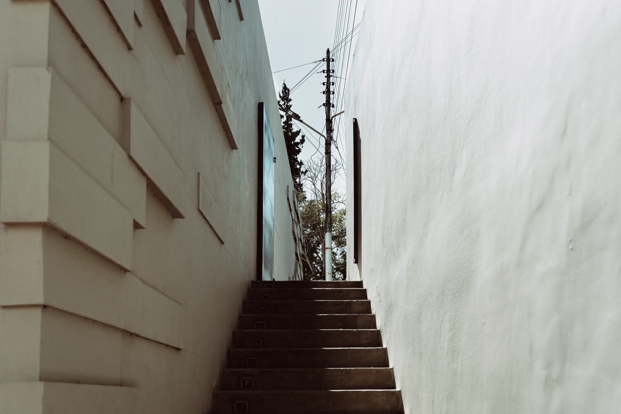 A narrow staircase climbing between two white walls toward a telegraph pole
