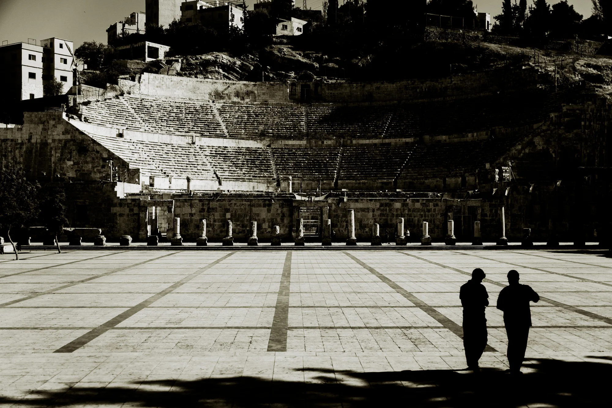 Two men in silhouette talking on the empty plaza in front of the Roman theatre in Amman