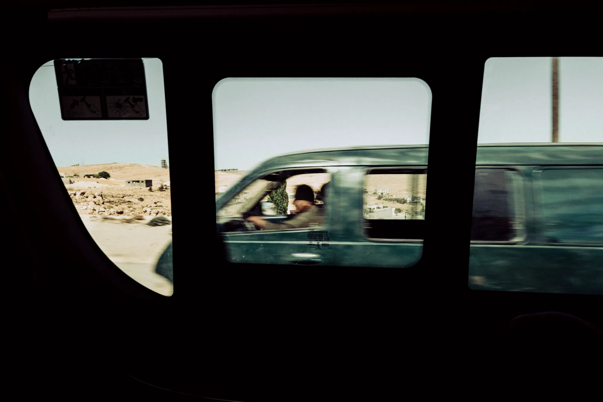 A blurred green van and its driver seen through the windows of a moving car