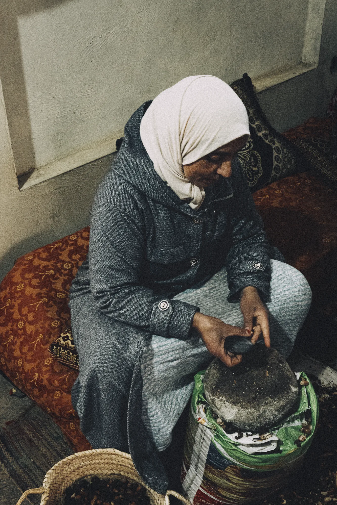 A woman in a headscarf grinding argan by hand on a stone mill