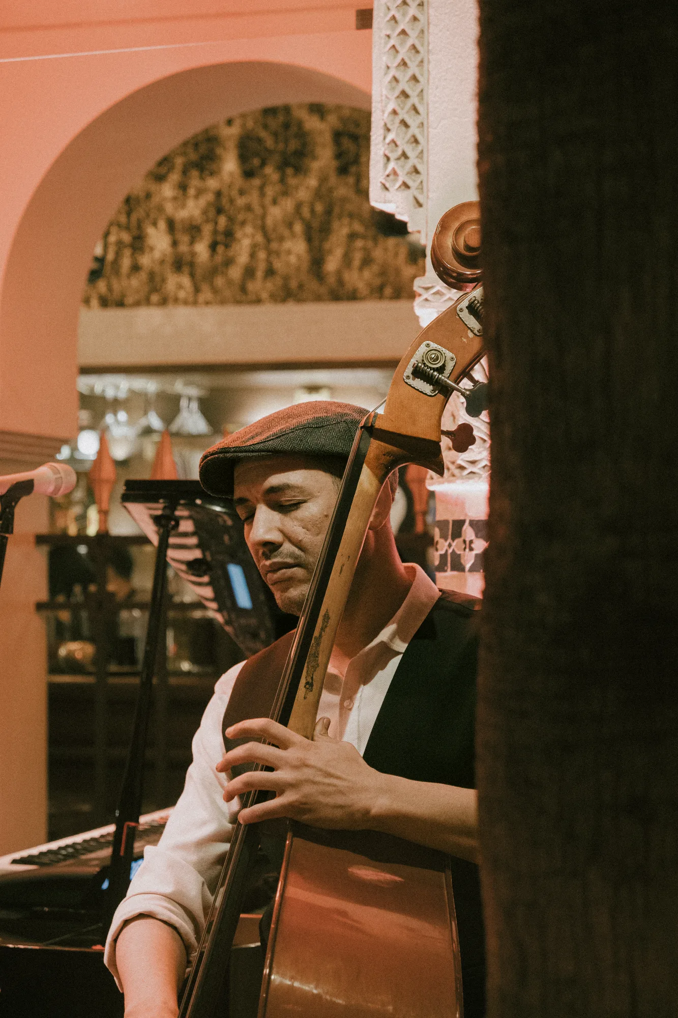 A musician in a flat cap playing double bass under a pink arch