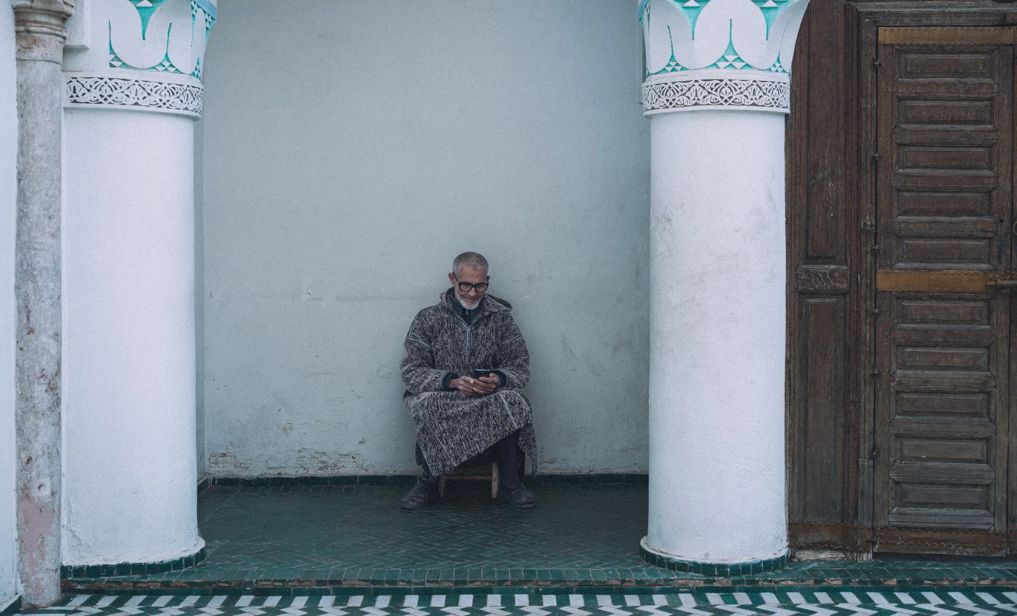 A man sitting on a step between two white columns, looking at his phone