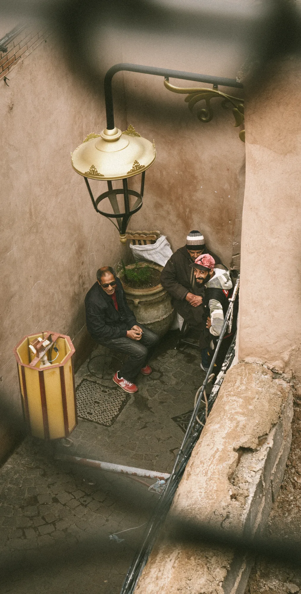 Three men sitting in a narrow corner of the medina, seen from above past an ornate street lamp