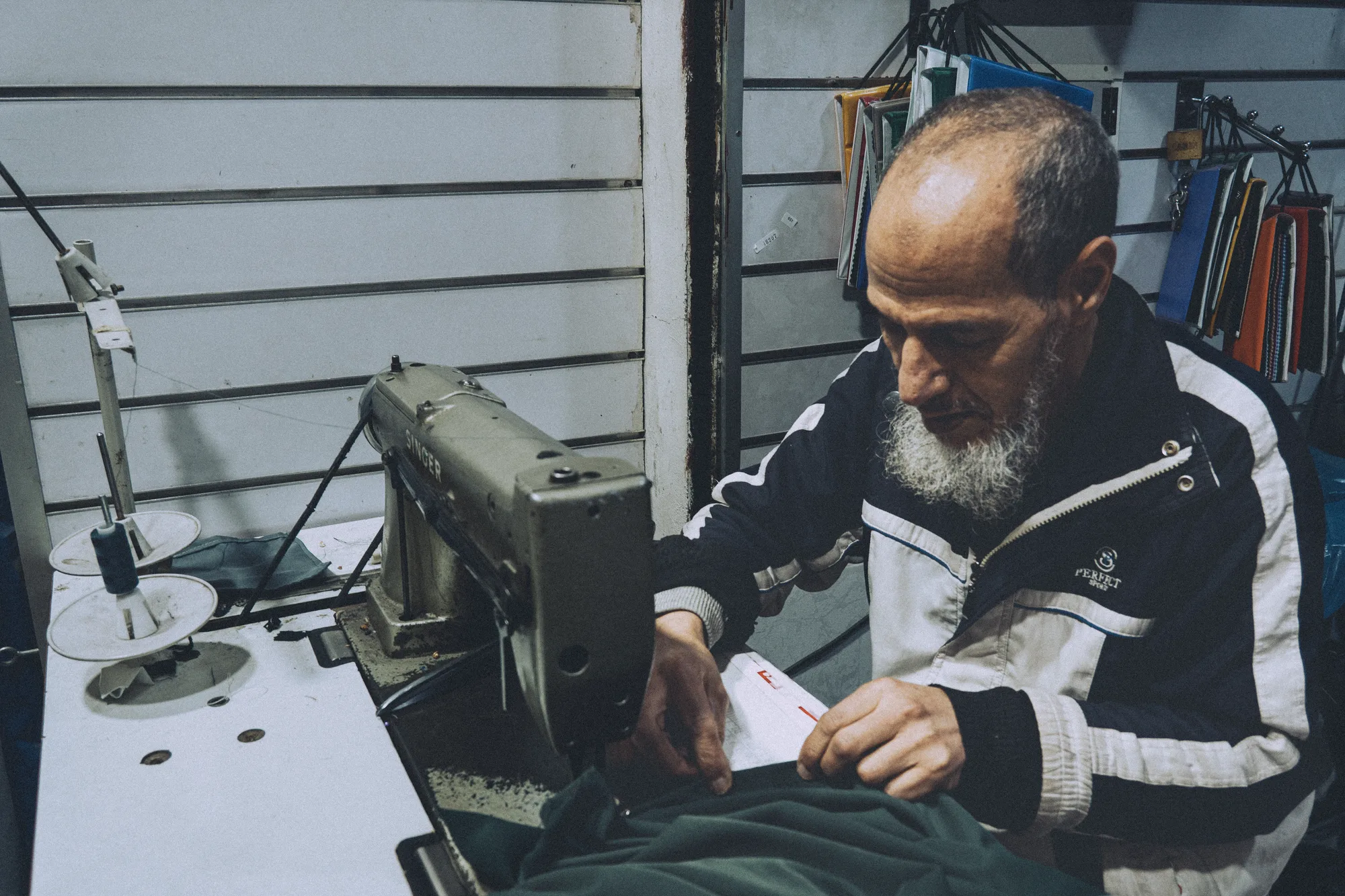 An older man working at a sewing machine in a small shop