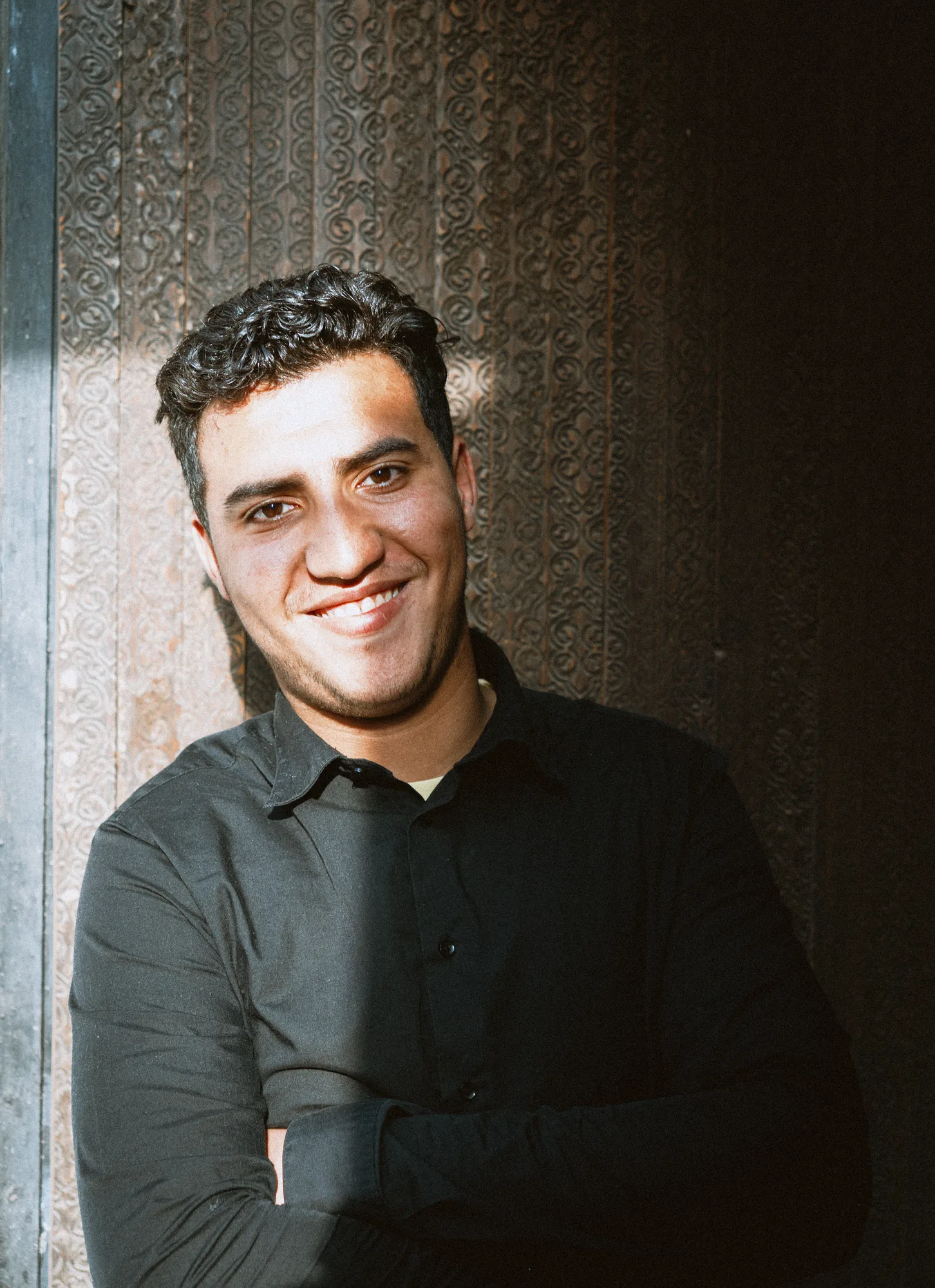 A man in a dark shirt smiling against a carved wooden wall