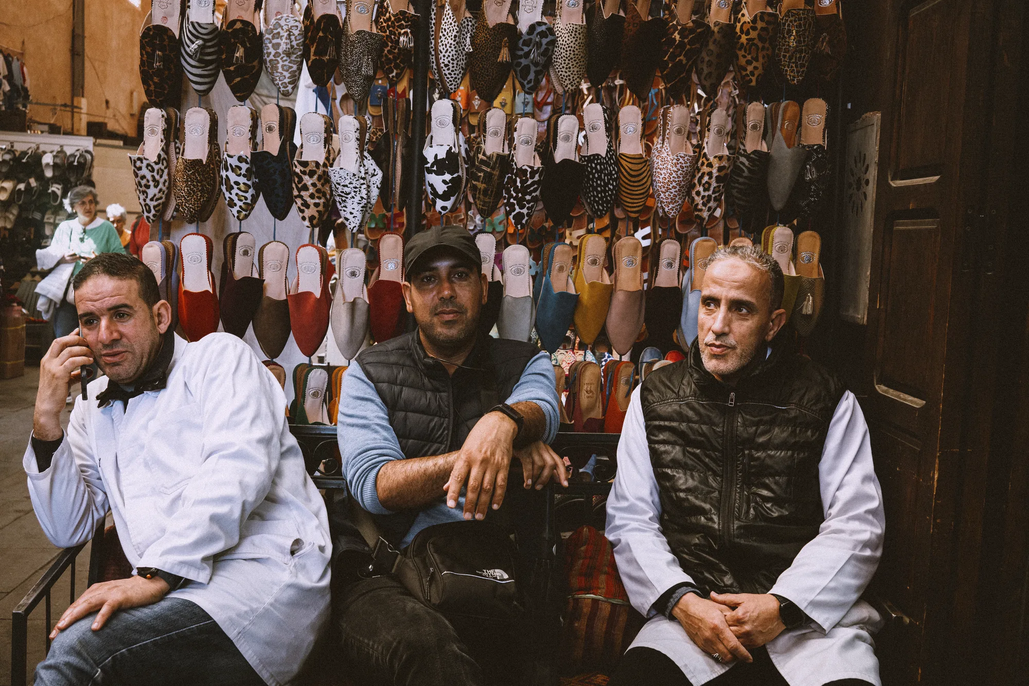 Three shopkeepers sitting in front of a wall of leather slippers