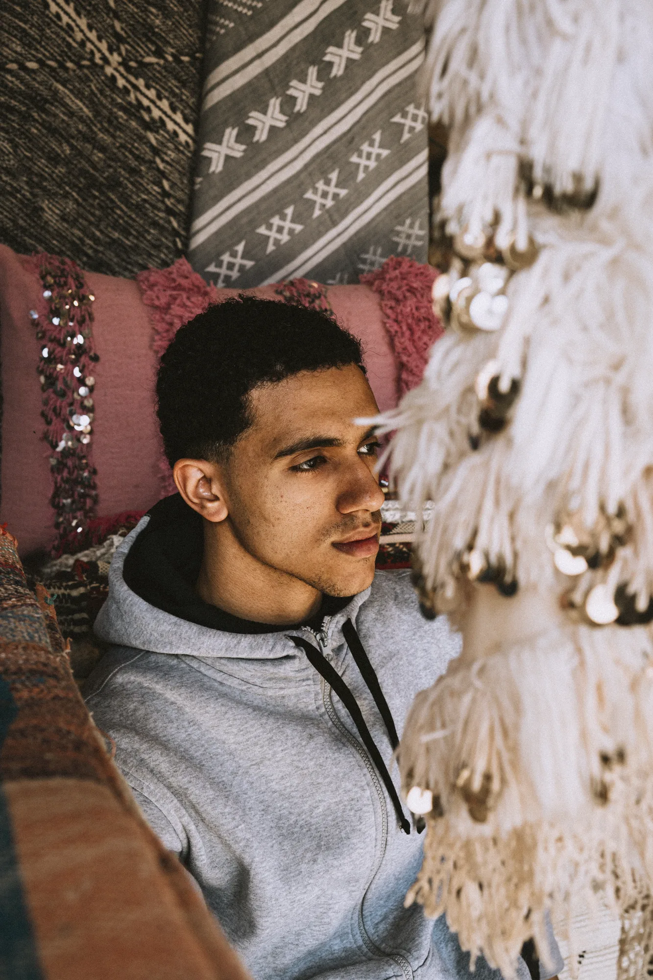 A young man in a grey hoodie between woven textiles and hanging tassels