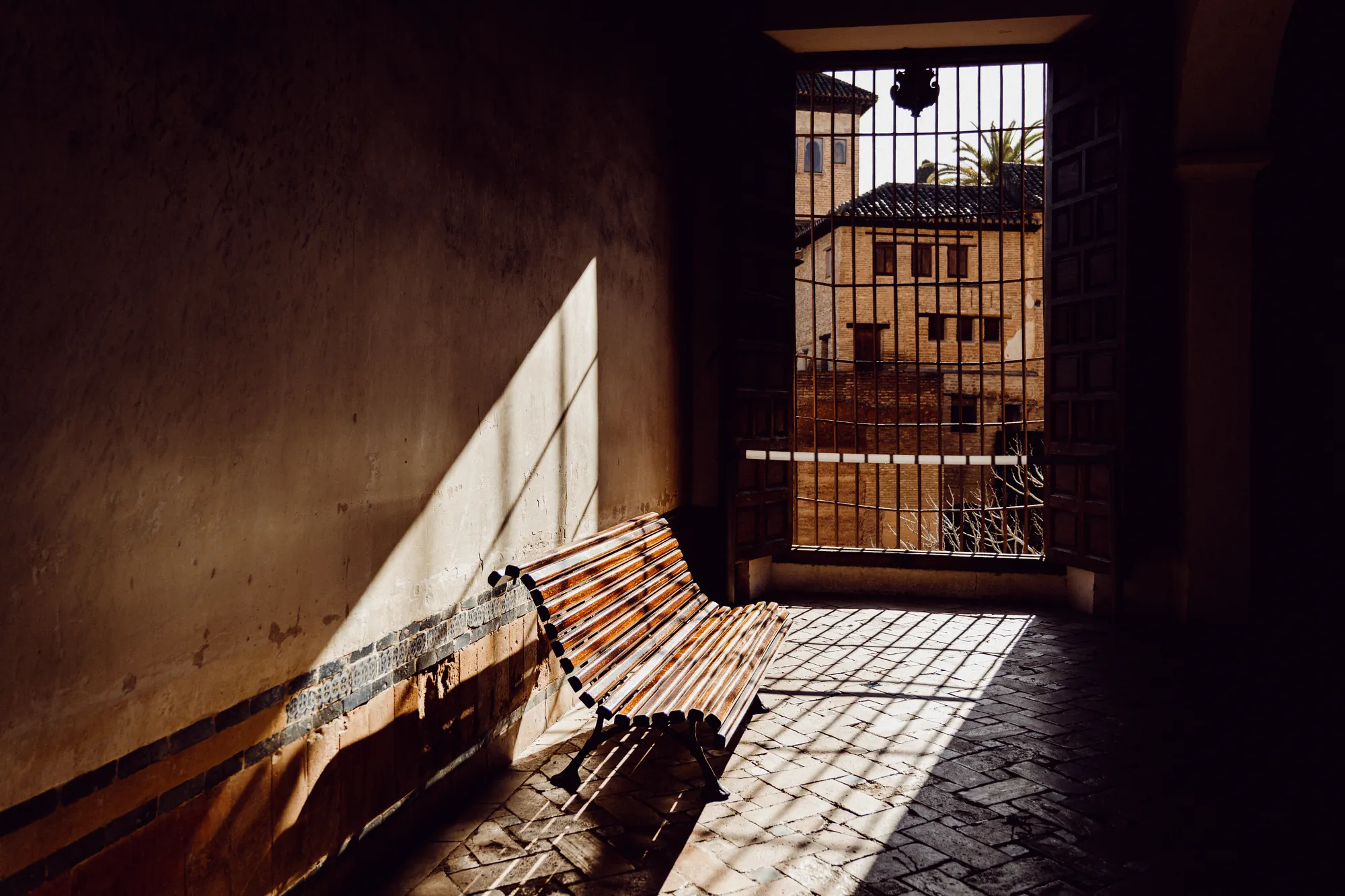 An empty wooden bench in a shaft of sunlight beside a barred window
