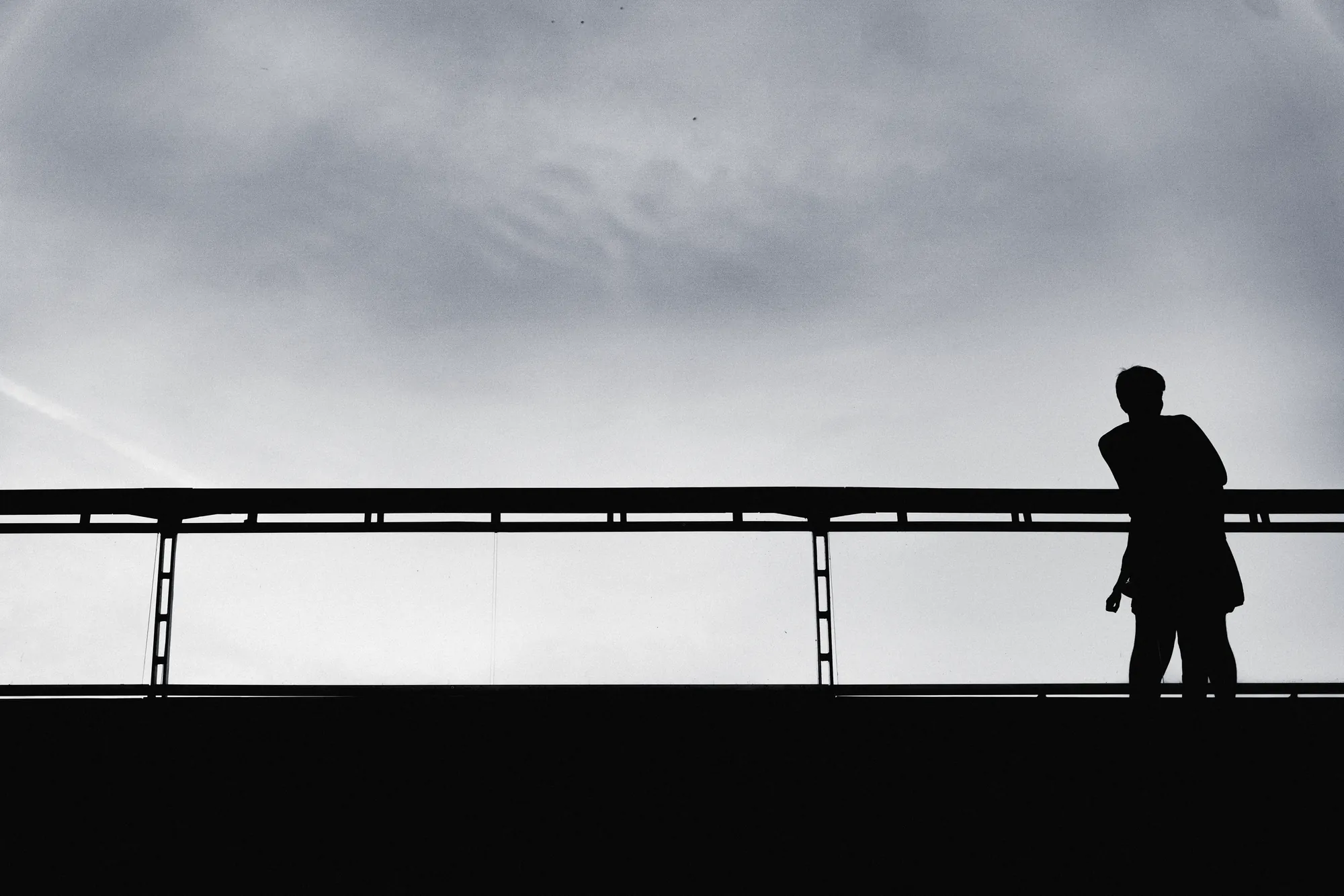 A lone figure silhouetted on a bridge against a pale sky