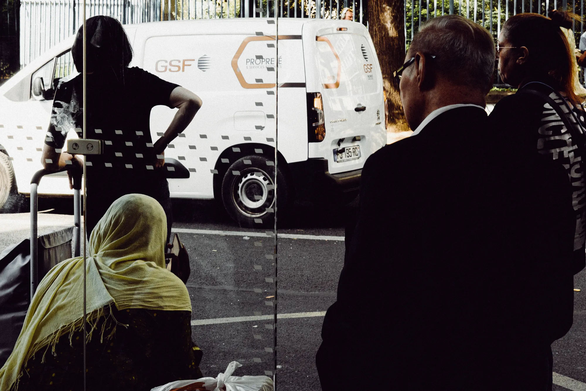 People waiting at a bus stop behind frosted glass, a white van beyond