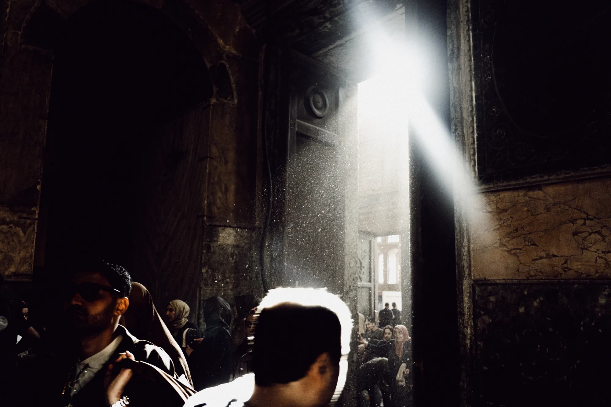 A shaft of light full of dust falling into a dark interior crowded with people