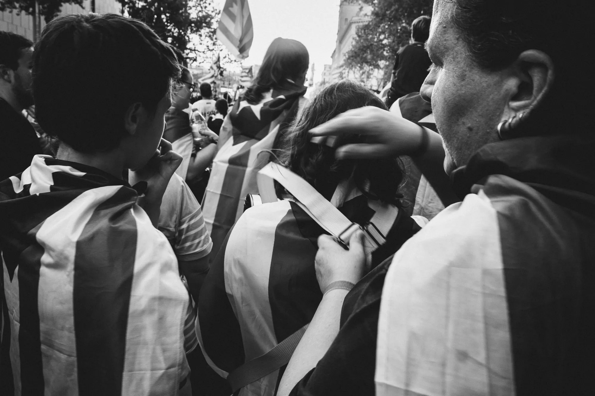 People wrapped in striped flags in a crowd, one adjusting another's hair
