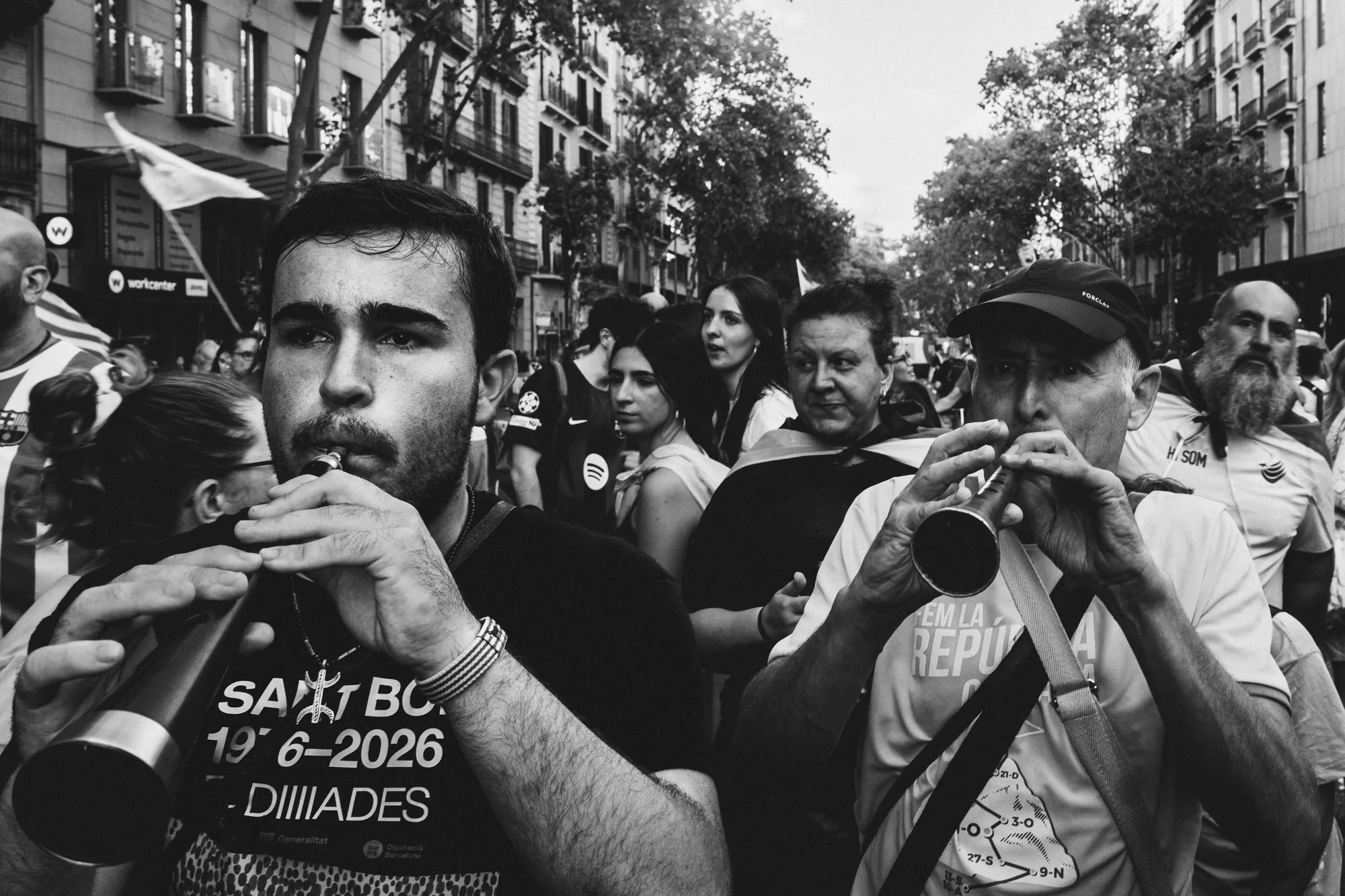 Two men playing wind instruments in a crowded street march in Barcelona