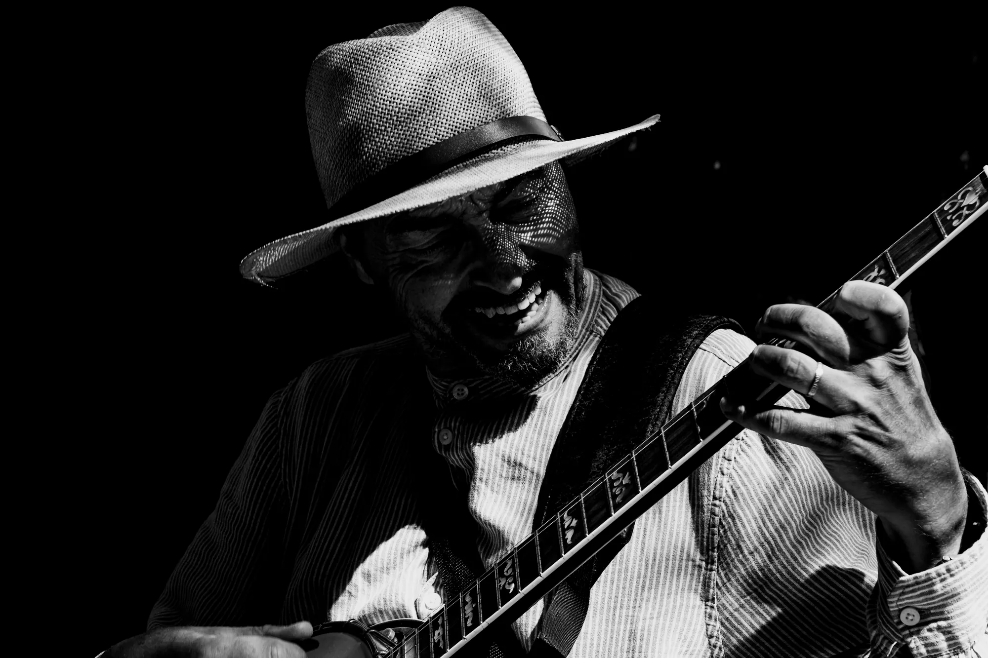 A street musician in a straw hat laughing as he plays, in hard light