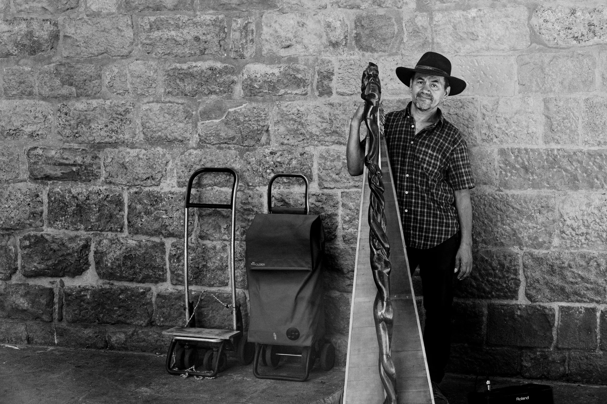 A performer with a tall instrument and two trolleys against a stone wall