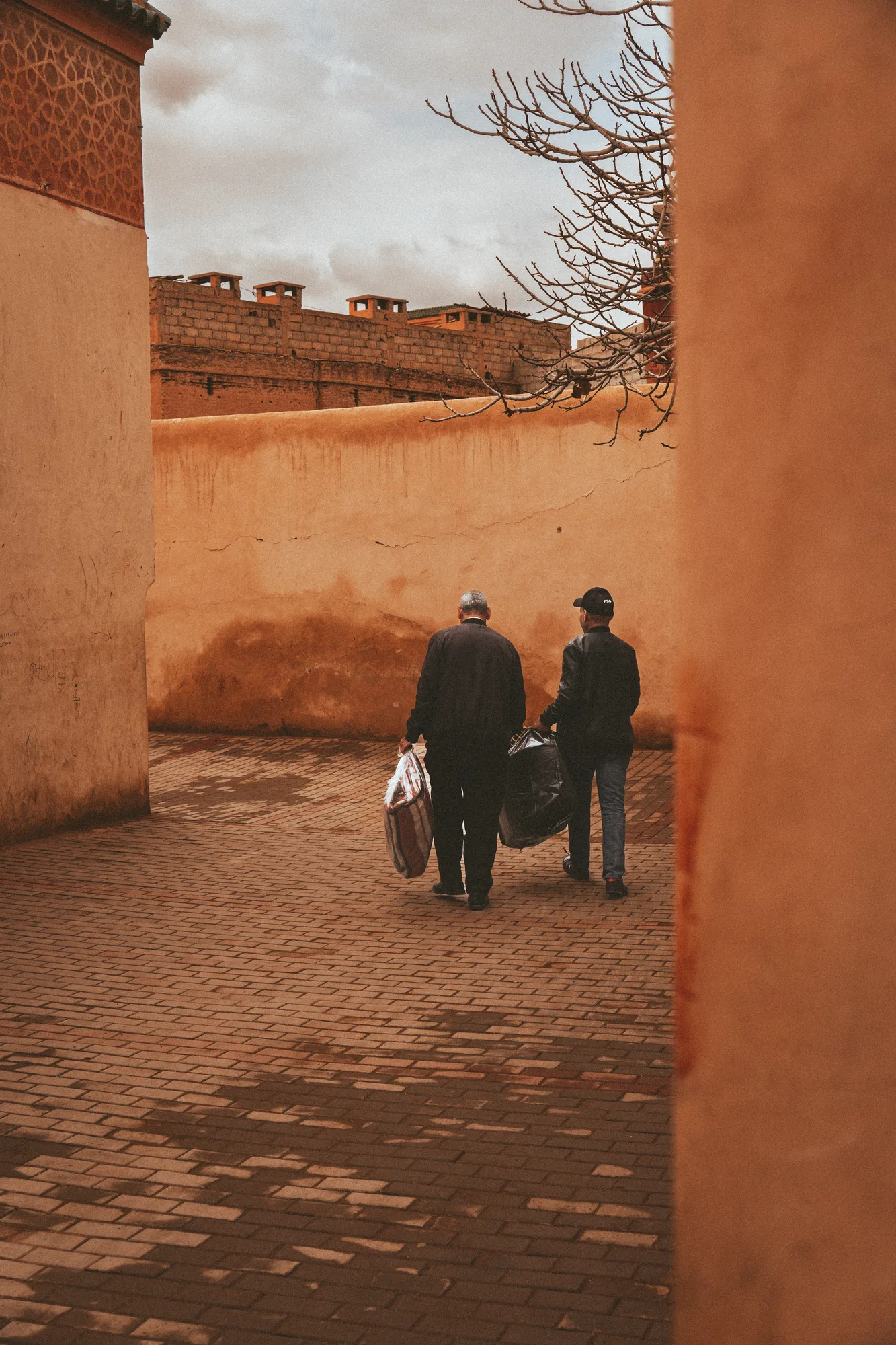 Two men carrying shopping bags walking away down an ochre alley
