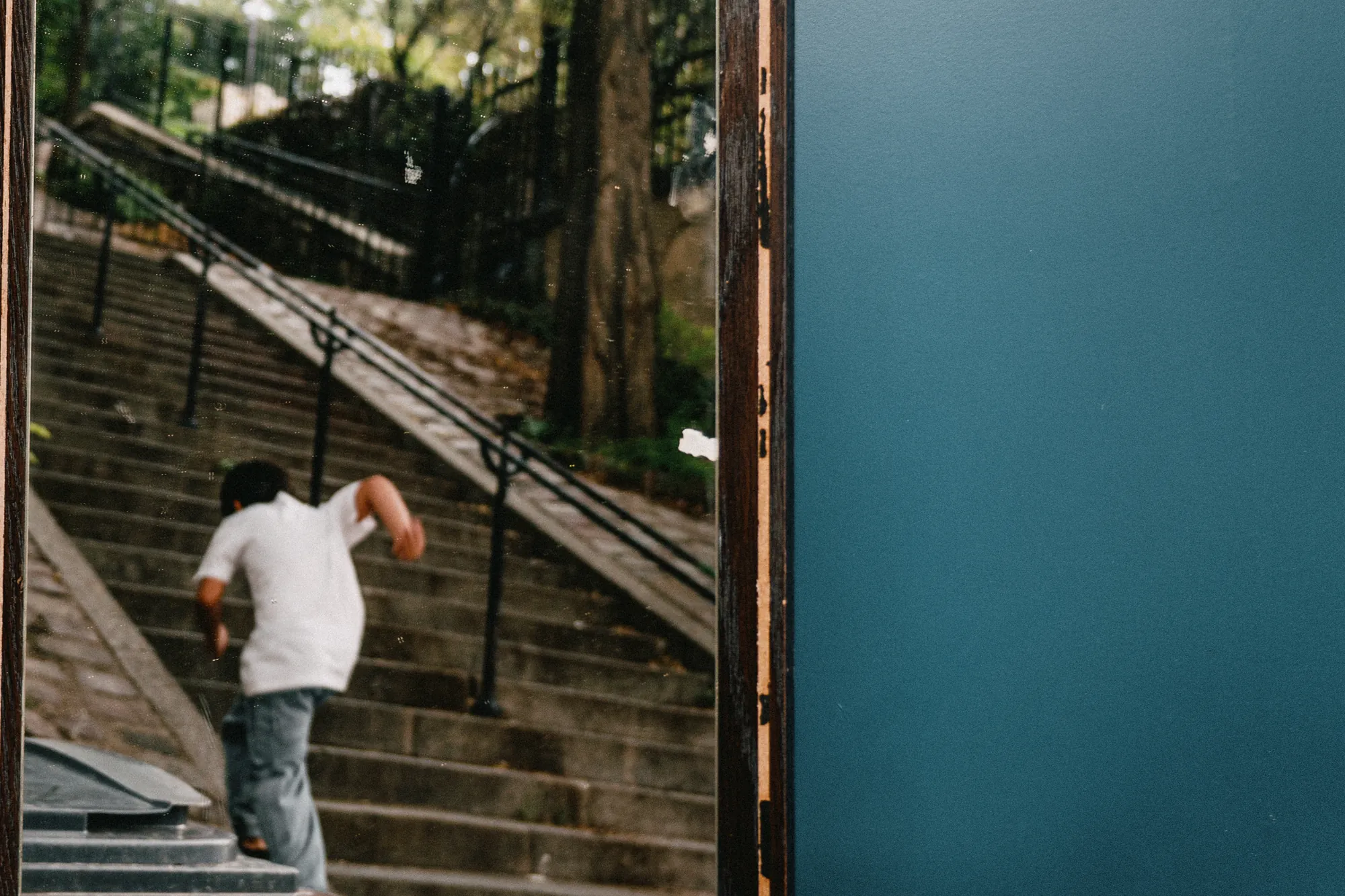 A boy climbing a staircase, seen in a mirror beside a teal wall